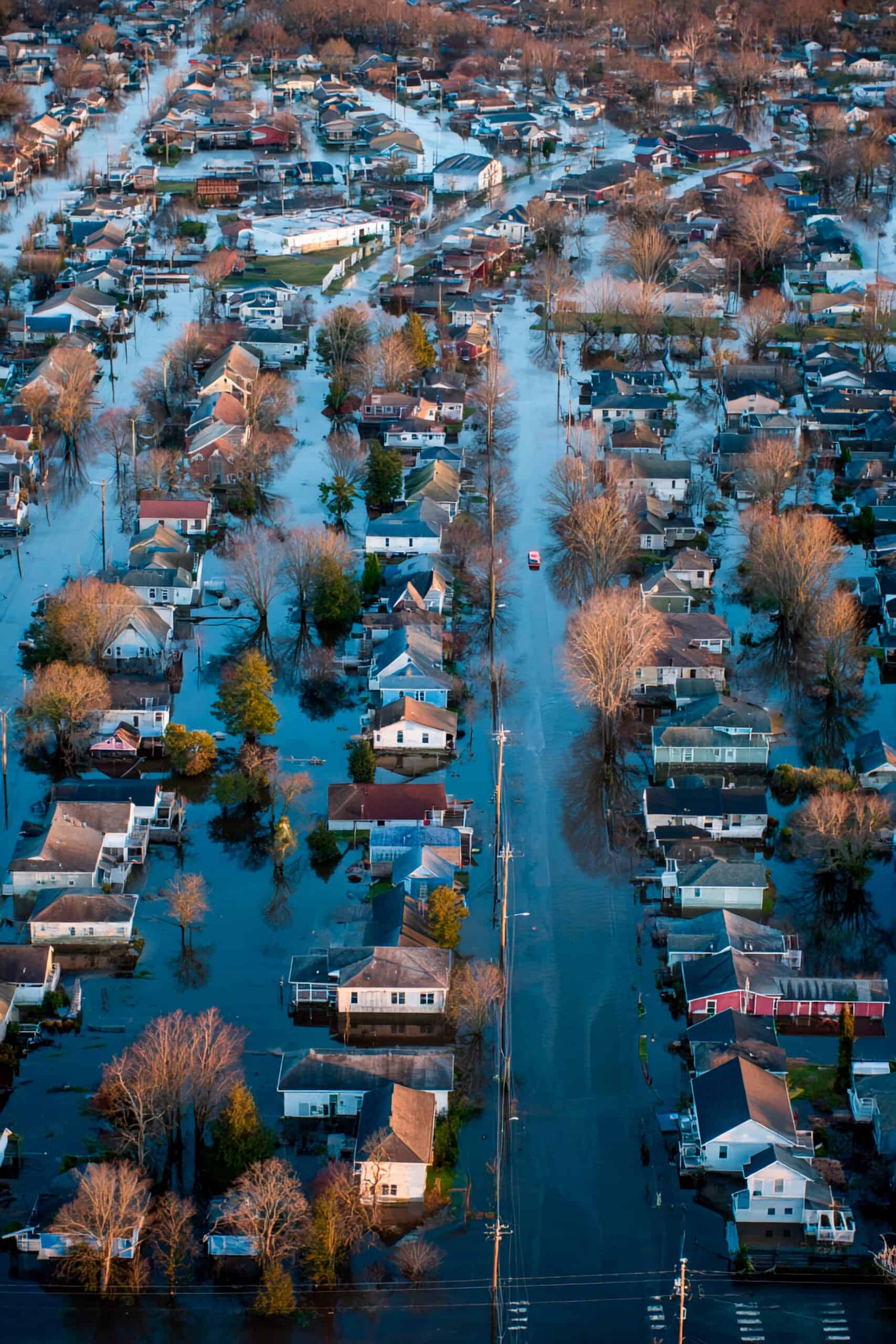 Water covers the streets and homes in a suburban neighborhood following a significant rainstorm. Trees are seen submerged, highlighting the severity of the flooding